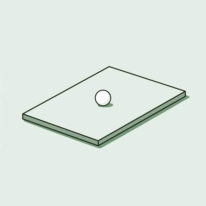 A plain flat rectangular board lying on the ground with a golf ball resting on it